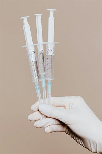 Gloved hand holding sterile syringes for medical use. (Pexels free to use photo)